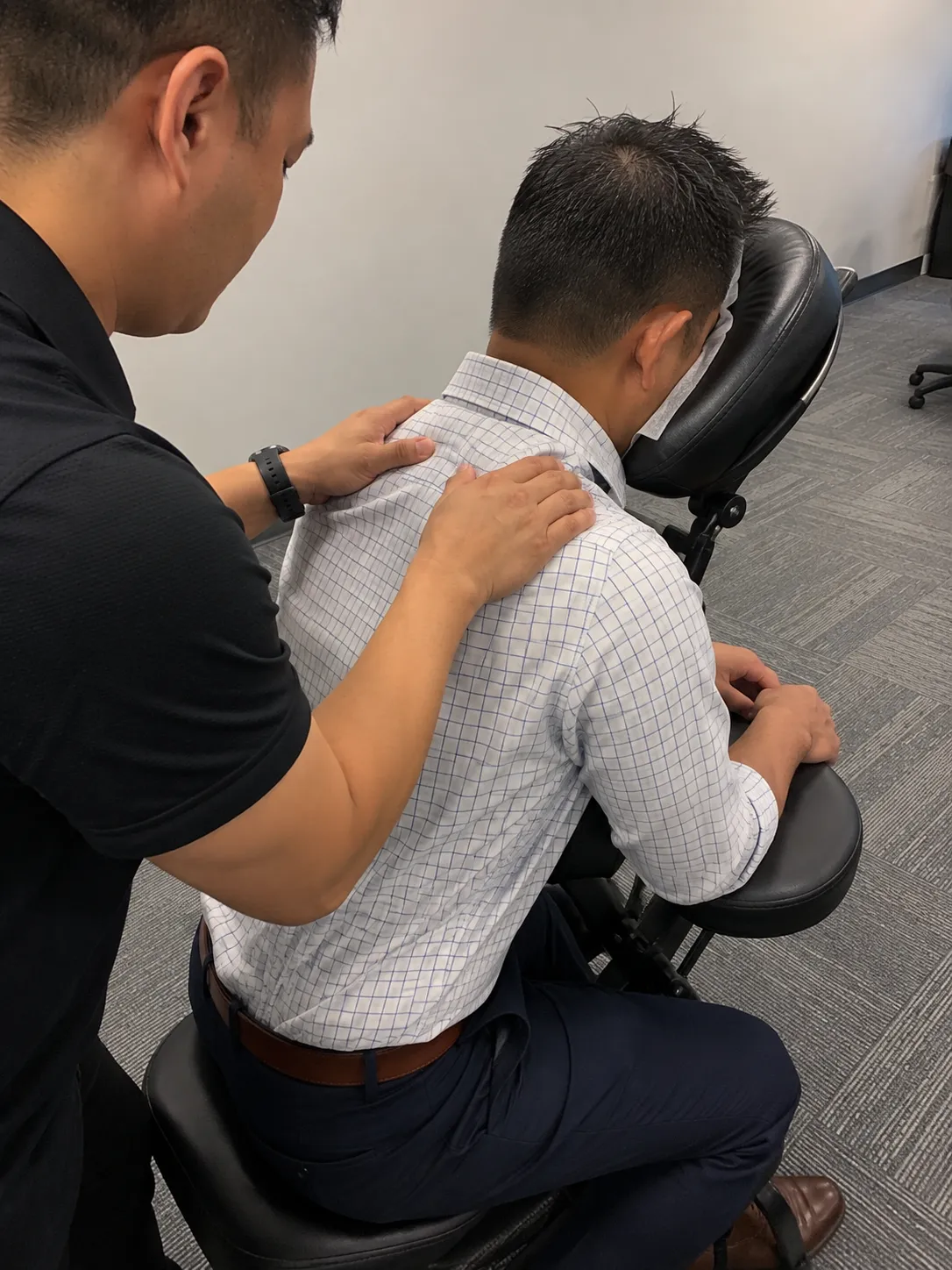Massage therapist working the shoulders of a fully clothed employee seated in a portable massage chair